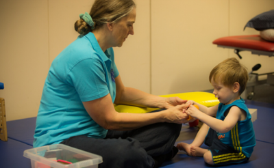 Therapist on the floor holding young boys hand