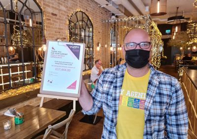 Photograph inside Mowgli Street Food Cardiff, a member of staff stands net to sign stating that they have raised over £7,4444.0.