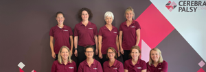 Photograph of therapy team (9 women) some seated, some standing, in front of Cerebral Palsy Cymru branded wall in our centre.