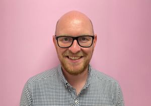 Photograph of of Head of retail in front of our pink wall.