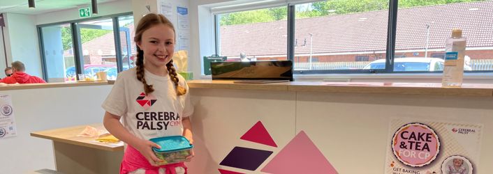 Photograph of young girl in Cerebral Palsy Cymru t-shirt, holding a box of cakes.